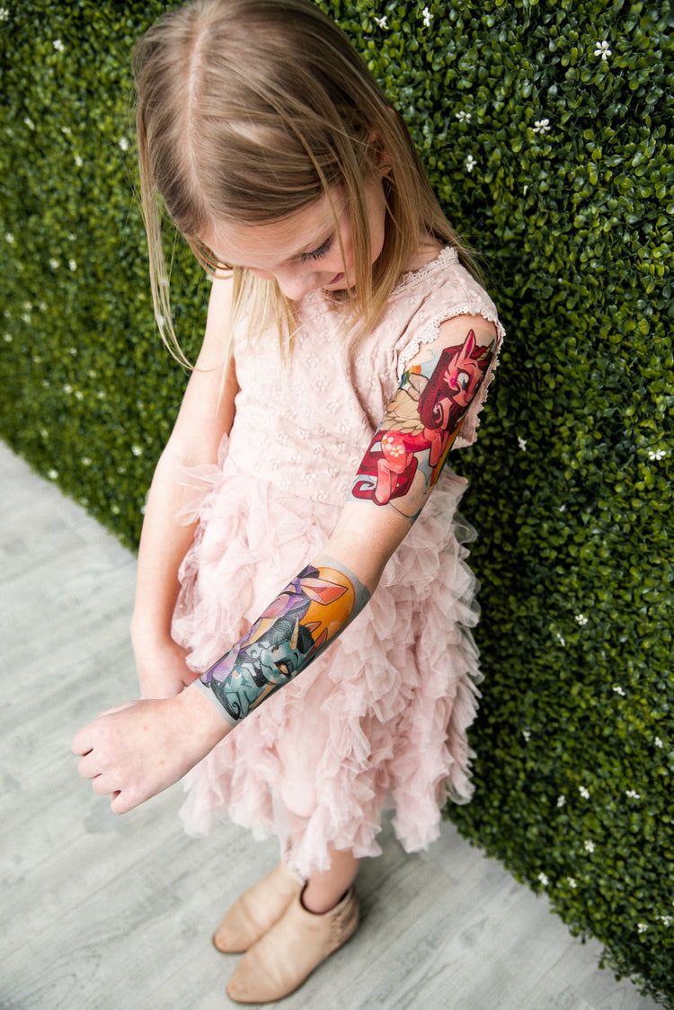 Little girl admiring her temporary tattoo sleeve from Tony Ray Tattoos with unicorns on it.