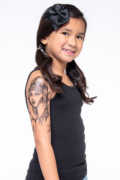 Young girl shows off upper arm sleeve of temporary tattoo depicting chicano style tattoo.