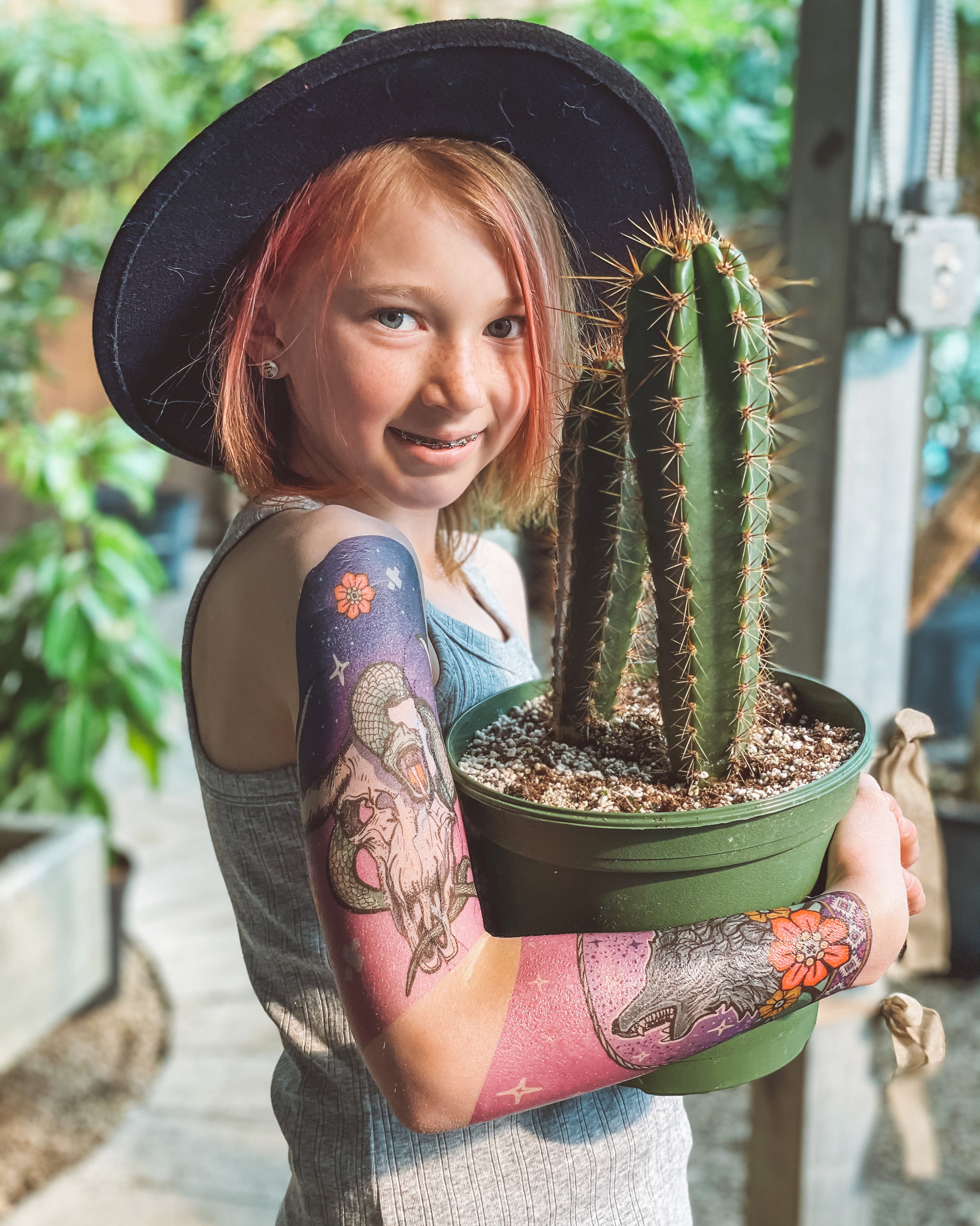 Young girl holding a cactus and showing off her Desert Oasis temporary tattoo sleeve.